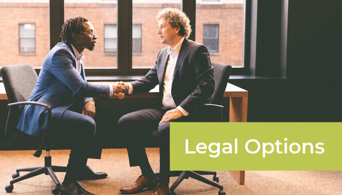 A professional man in a business suit shaking hands with another man across an office desk.