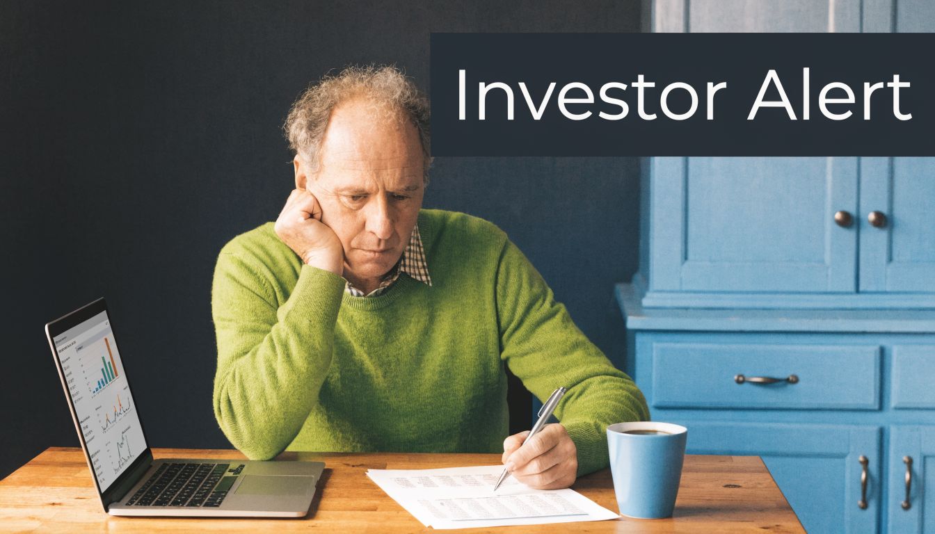 An older man sitting at a desk looking concerned while reviewing financial documents and laptop data.