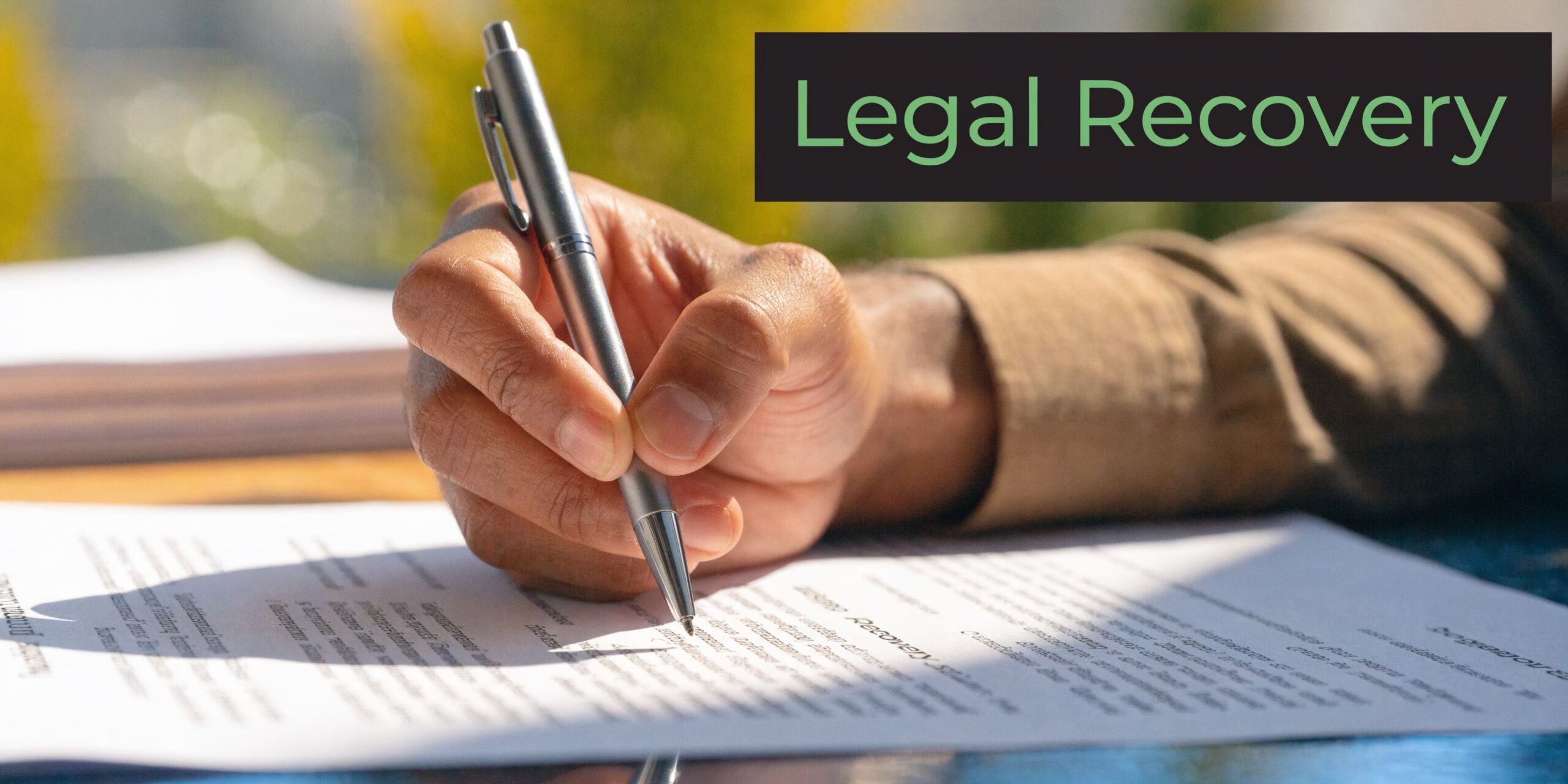 A close-up of a person's hand using a silver pen to sign a document labeled Legal Recovery.