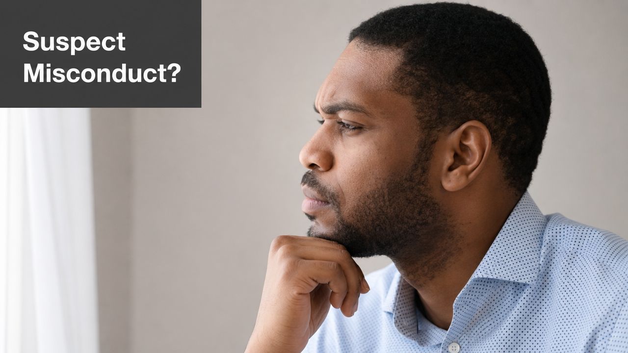 A pensive man in a blue patterned shirt looking away while resting his chin on his hand.